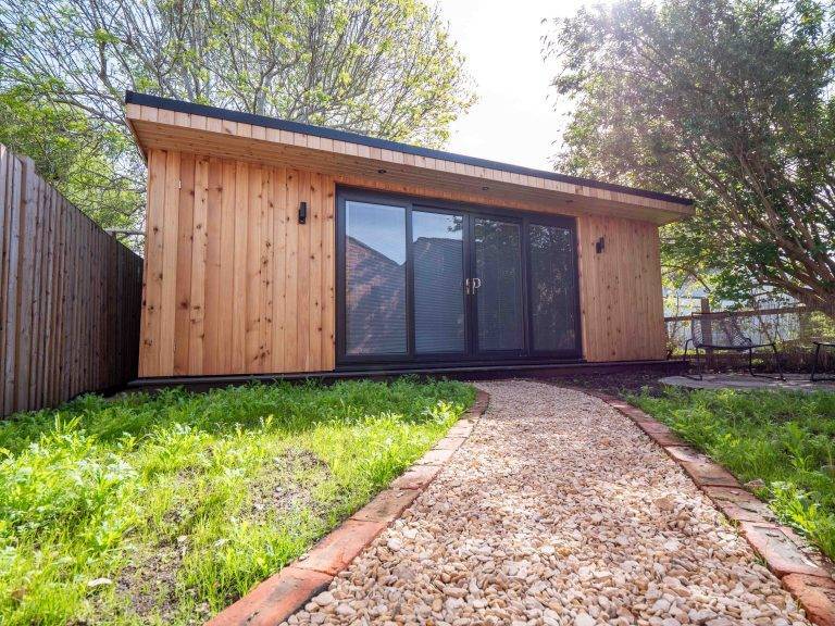 Cedar-clad garden guest house with sliding doors at the end of a gravel path