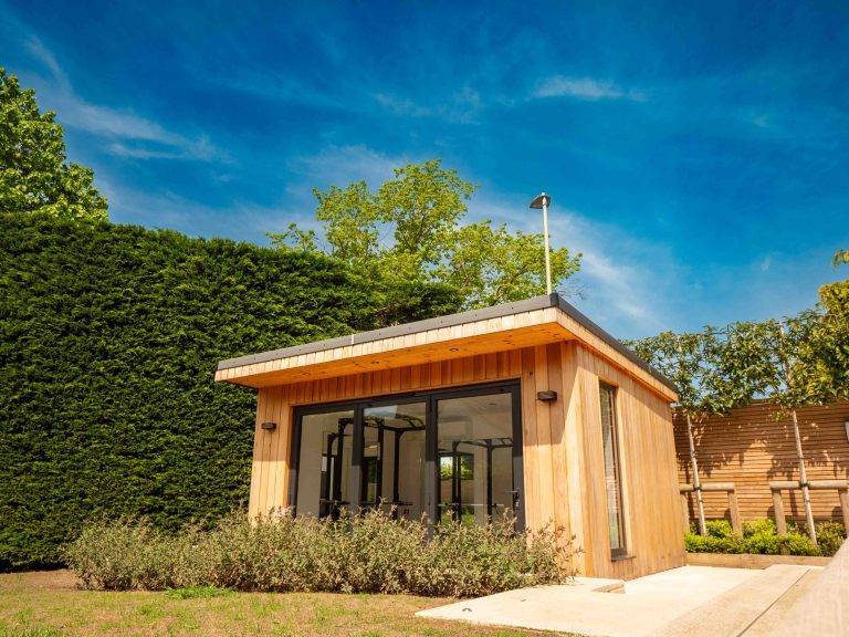 Cedar-clad garden gym with bifold doors set against a tall hedge