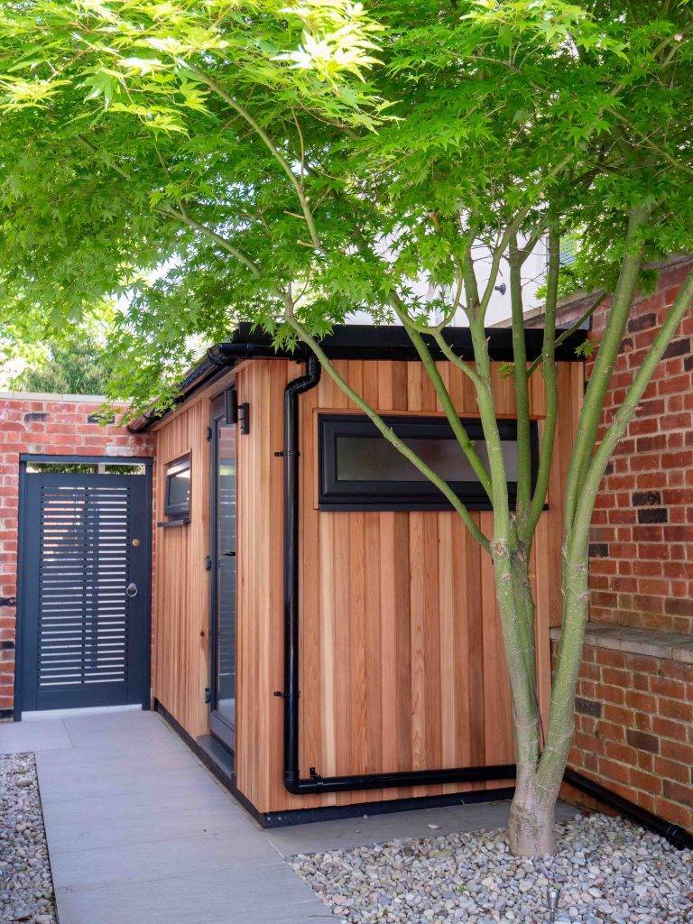 Cedar-clad garden room with an anthracite door and windows beside a side path