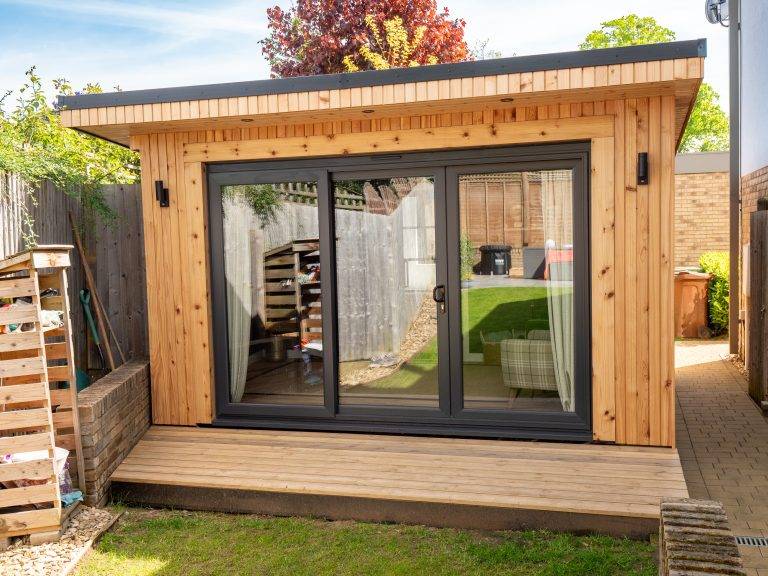 Cedar-clad garden room with grey bifold doors on timber decking