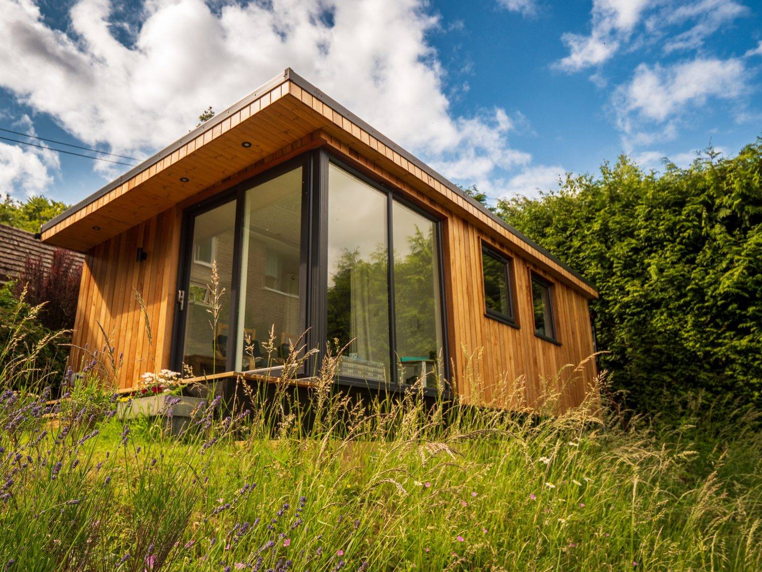 Cedar garden room with a pitched roof and glazed gable in a meadow garden